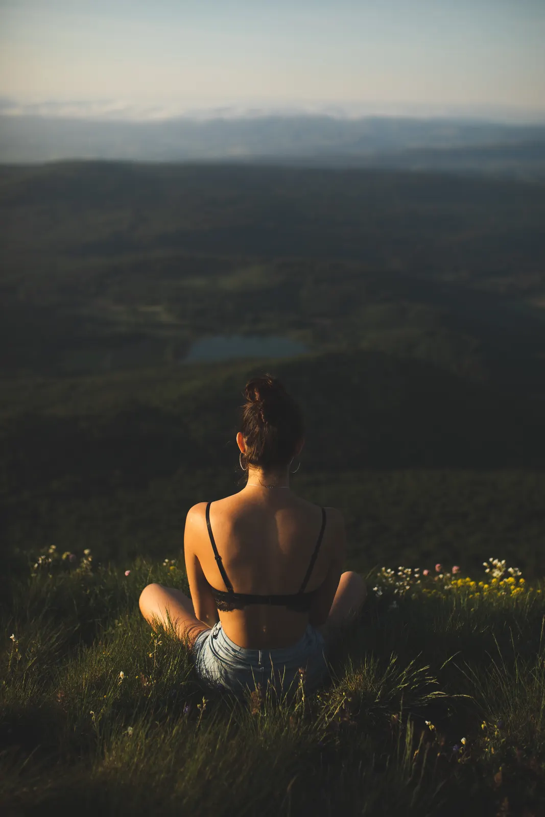 Mujer sentada de espaldas en la hierba frente a un paisaje al atardecer